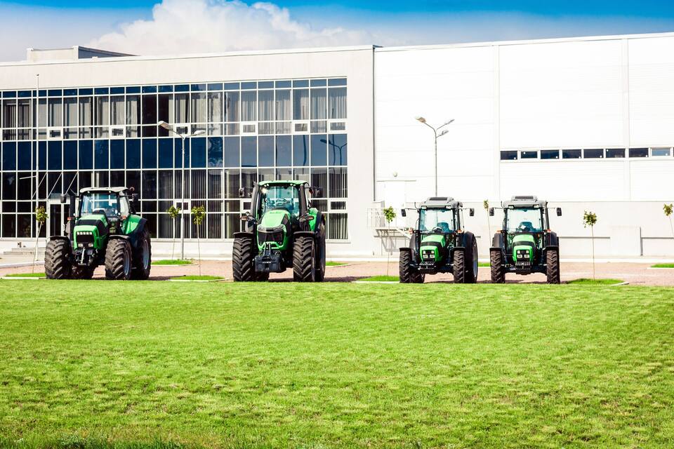 Three green tractors parked in front of a modern building with large windows.