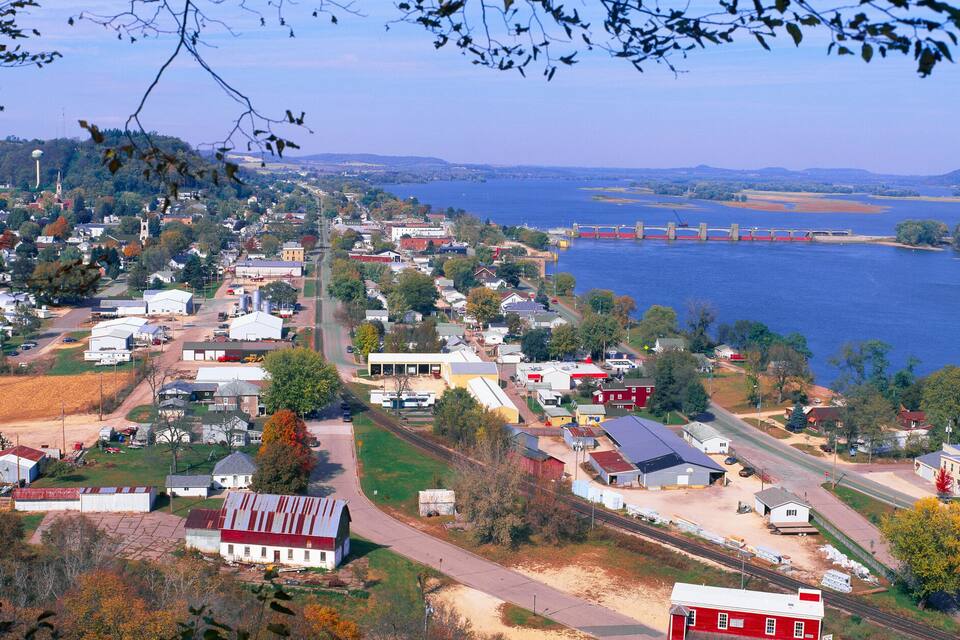 A town by a river with a bridge, houses, and farmland.