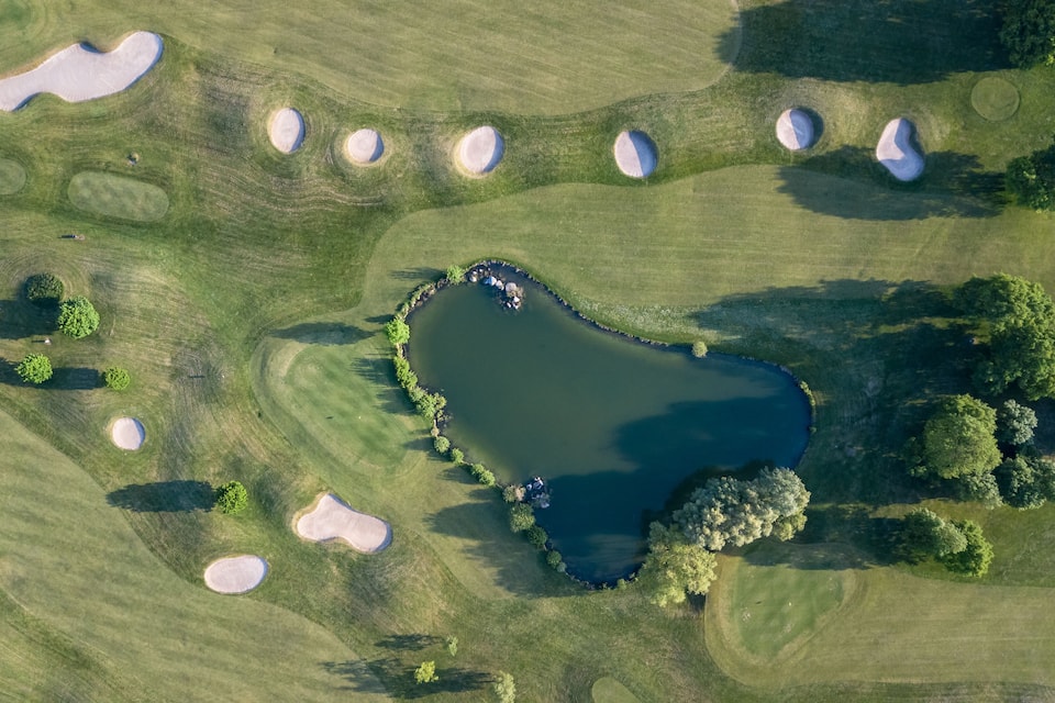 Vista aérea de um campo de golfe com lago, áreas de areia e árvores.