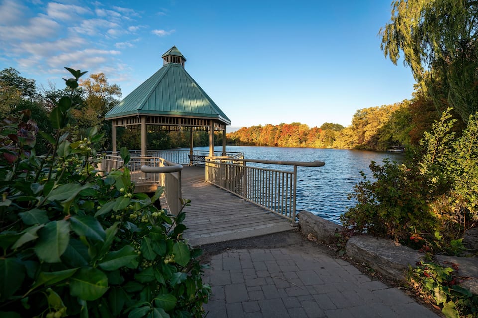 A gazebo by a lake surrounded by autumn foliage.