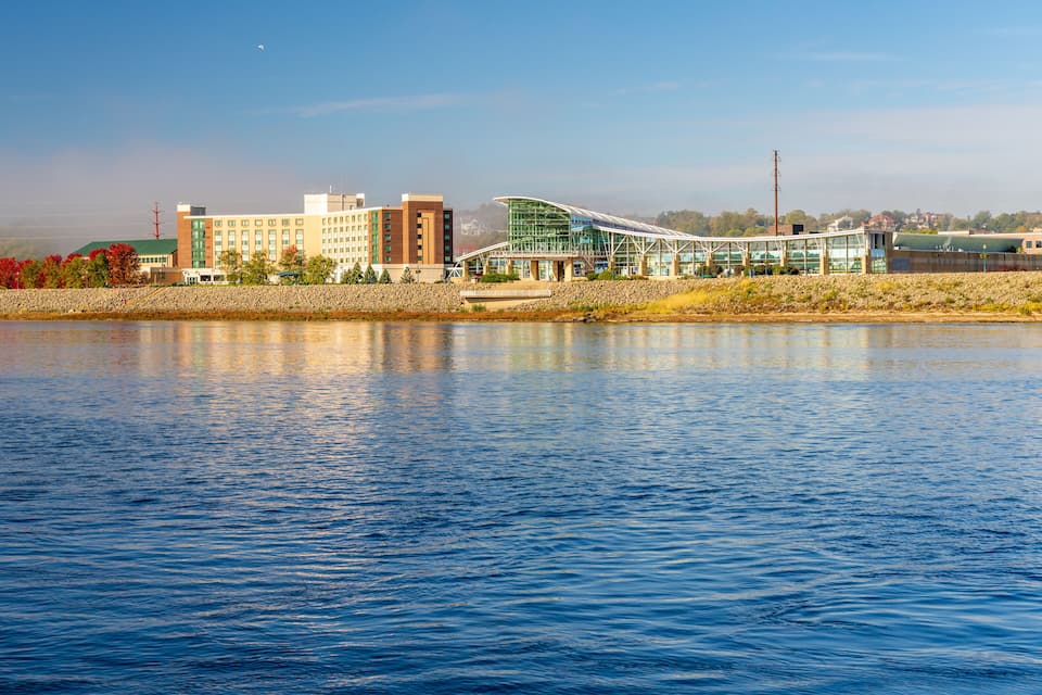 Un paisaje marítimo con edificios, incluyendo una estructura moderna de vidrio, y agua tranquila que refleja los edificios.