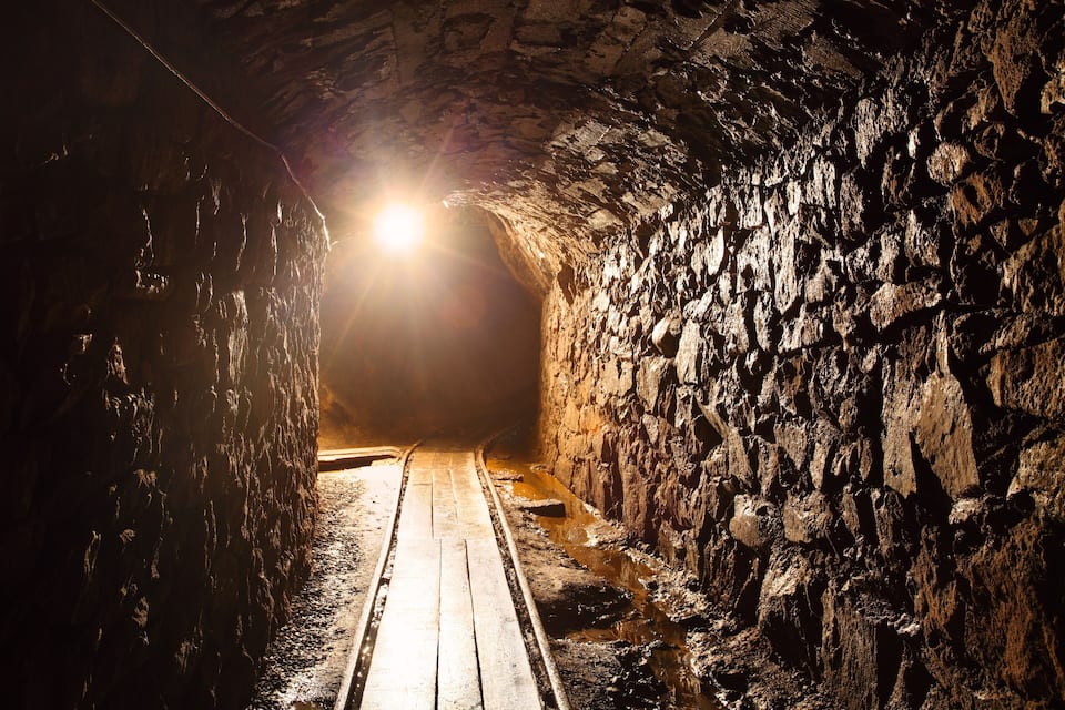 Un tunnel stretto e poco illuminato con pareti in pietra grezza e un percorso in legno.