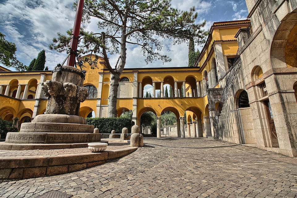 Un patio con una fuente de piedra, edificios amarillos con arcos y un cielo despejado.