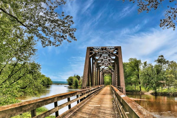 Beneath a blue sky with white clouds on a summer day in Wisconsin, an old train trestle has been converted to carry only hikers and bikers across a Mississippi backwater on the Great River Trail.