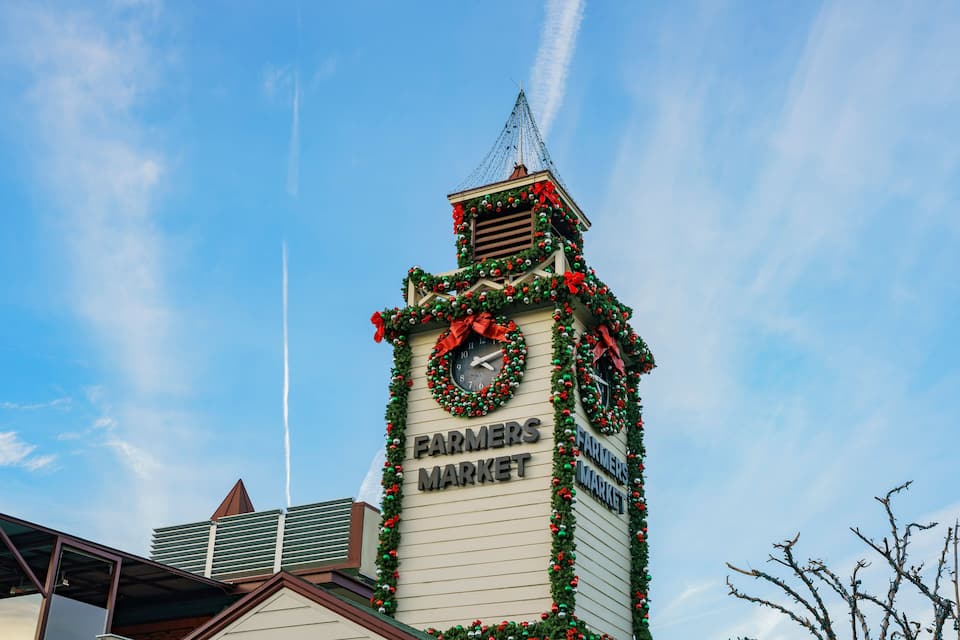 A building with a clock and the words "Farmers Market" on it, decorated with Christmas garlands and ornaments.