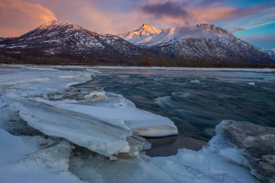 Un río congelado con témpanos de hielo, montañas cubiertas de nieve y un cielo despejado.