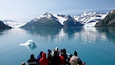 A group of people on a boat observing a glacier in a mountainous lake.