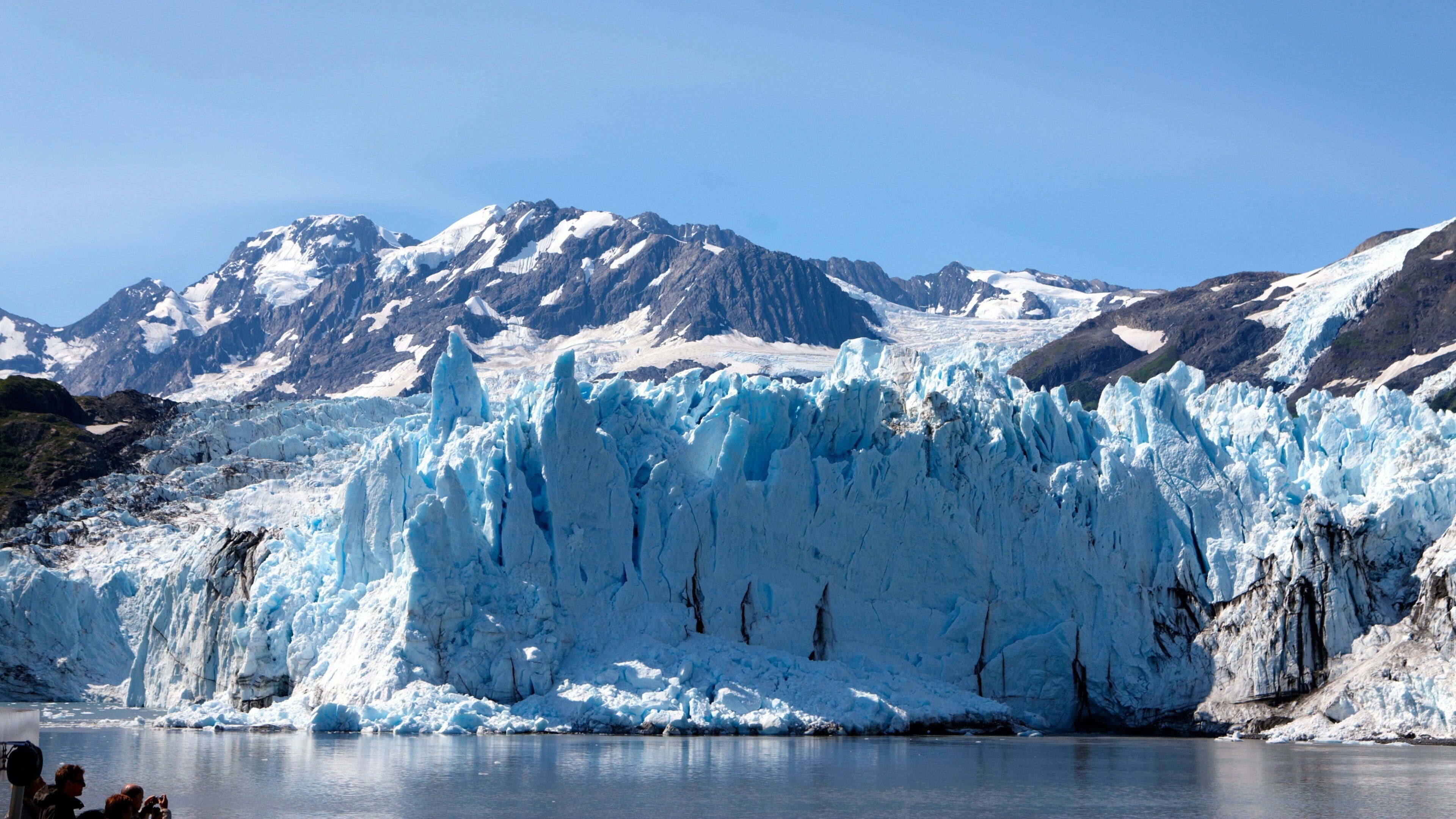 A glacier with a large ice face and a calm lake in the foreground.