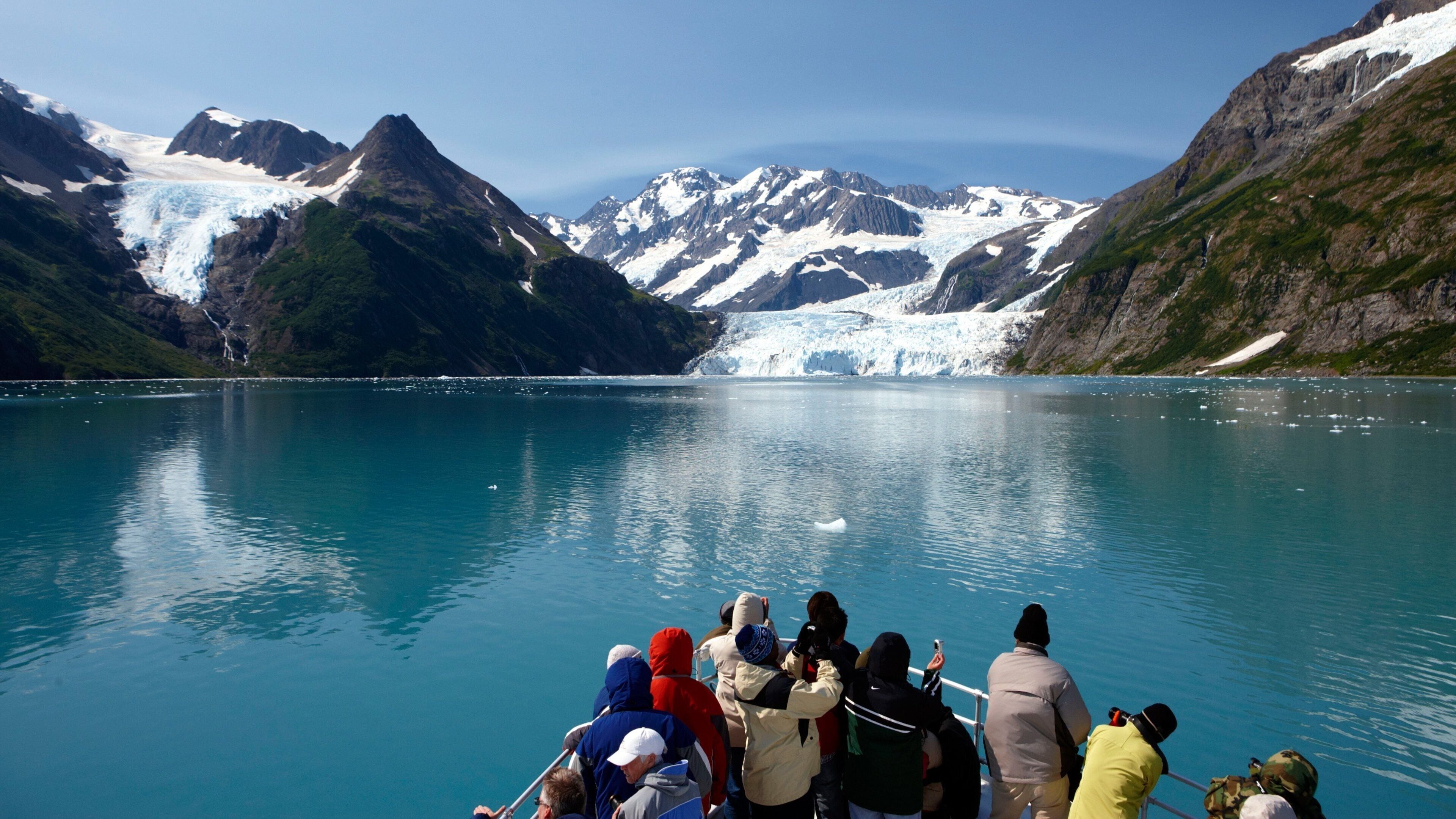 A glacier in a mountainous landscape with a group of people on a boat in the foreground.