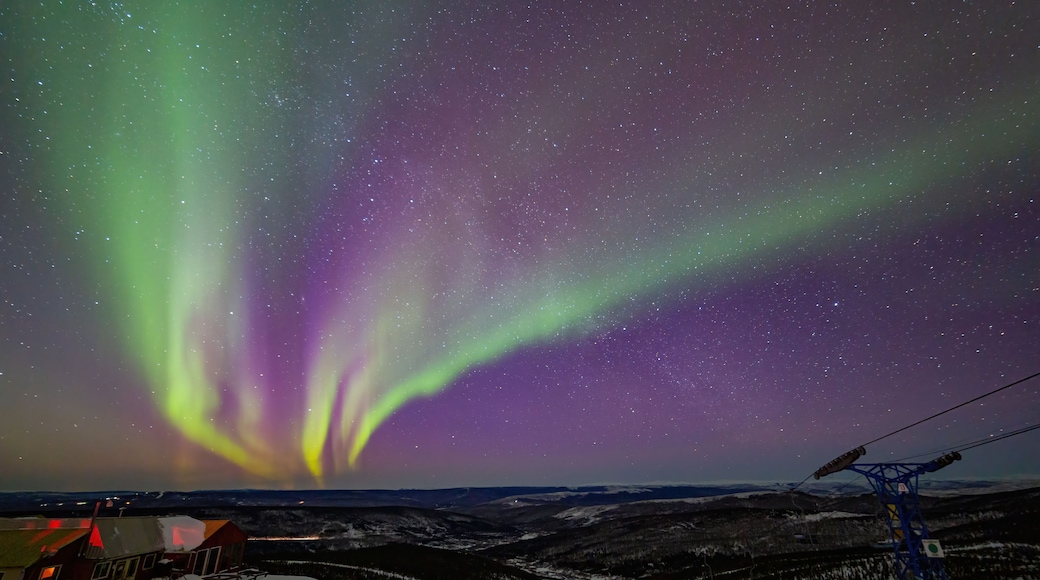 The Northern Lights over a snowy landscape with a cabin and power lines.