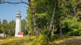 A white lighthouse with a red roof, surrounded by dense green trees and a clear blue sky.