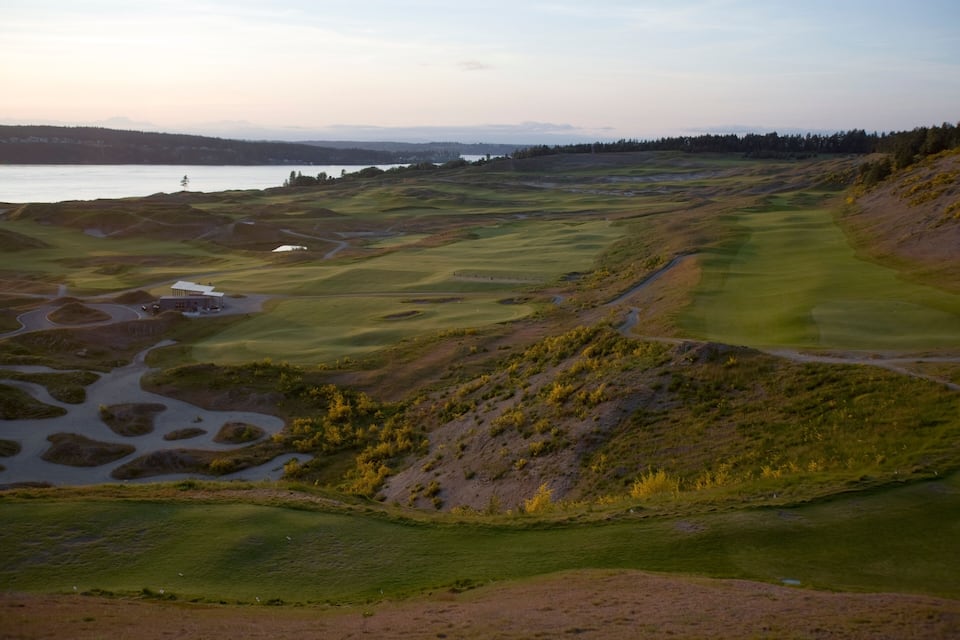 Ein Golfplatz mit See, sanften Hügeln und einer entfernten Skyline der Stadt.