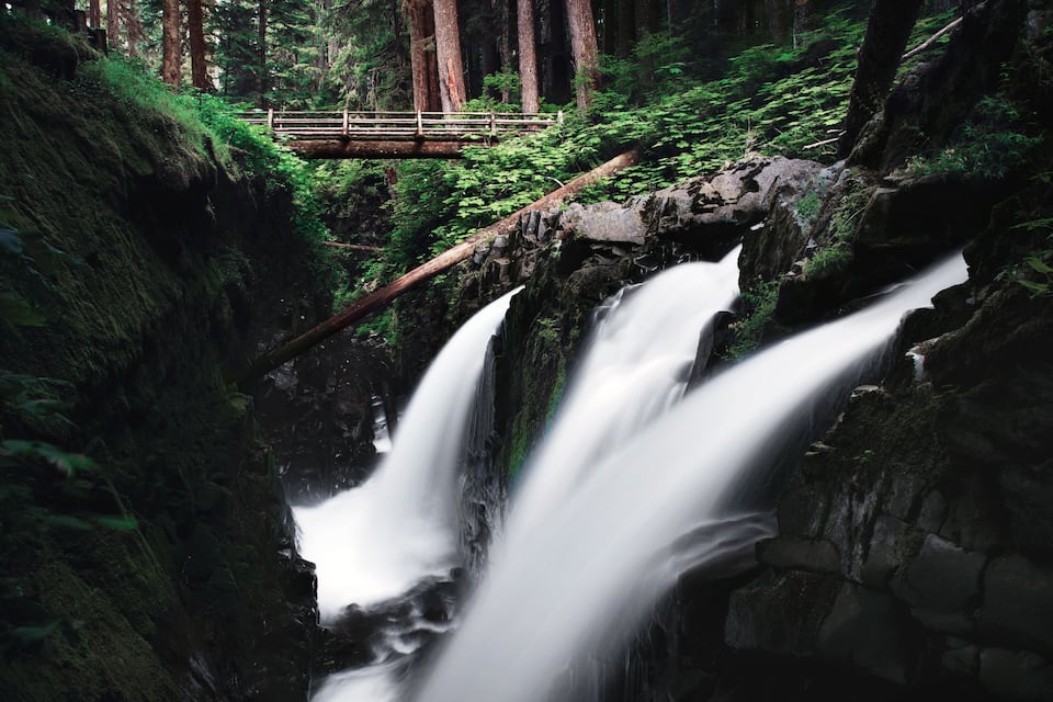 Una cascada en un bosque con un puente de madera.