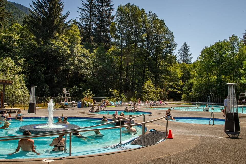 Una piscina pública envoltada d'arbres amb un paisatge de muntanyes al fons.