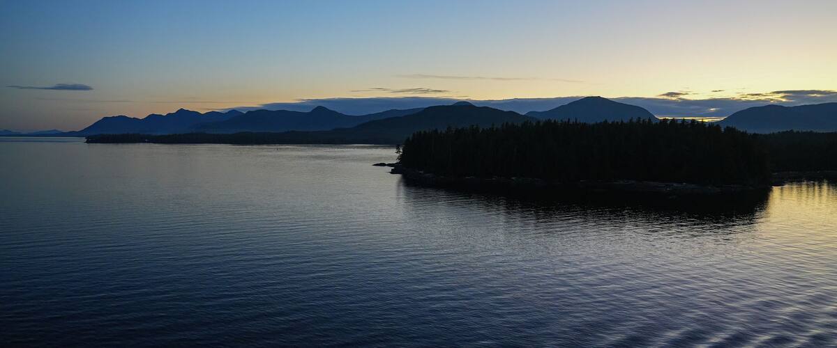 A calm lake with a small island of trees in the center, surrounded by mountains under a clear sky.