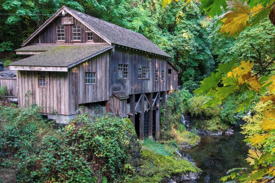 A wooden house on stilts by a river surrounded by dense foliage.