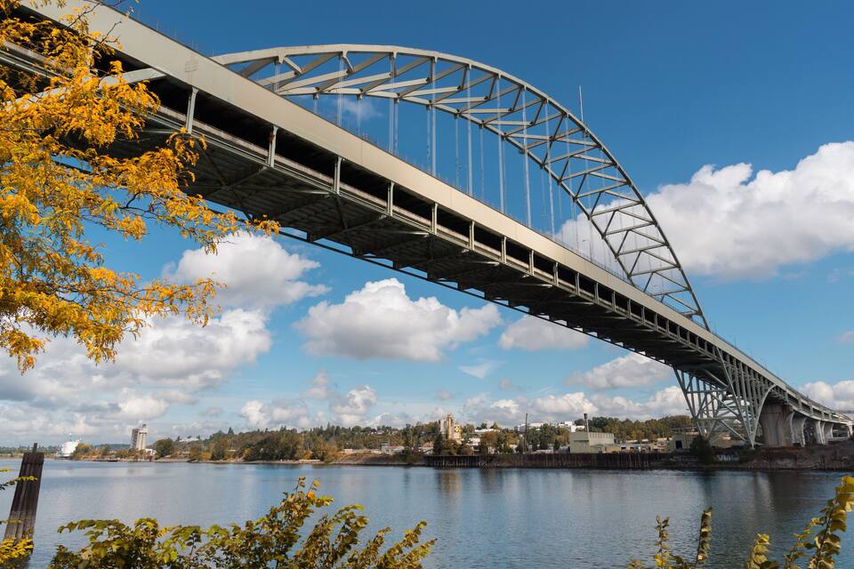 Un gran puente de acero que cruza un río, con cielo despejado y follaje otoñal.