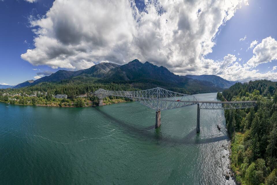 A suspension bridge over a river, surrounded by mountains and dense forests.