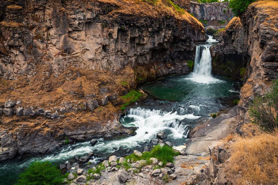 A waterfall cascading down a rocky gorge with a river flowing through it.