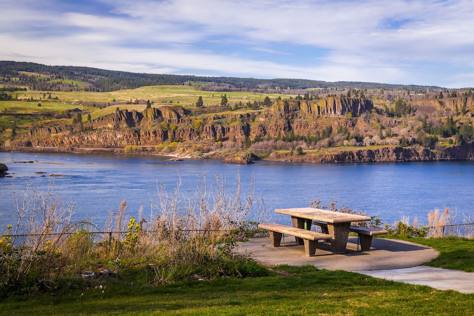 A picnic table by a lake with cliffs in the background.