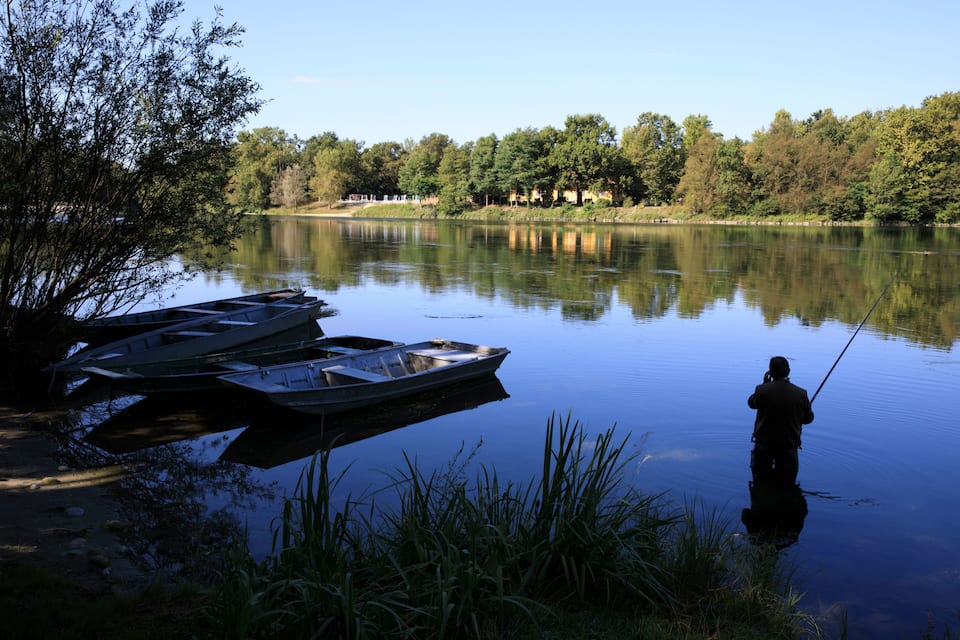 Un lago tranquilo con barcos amarrados en la orilla y una persona pescando.