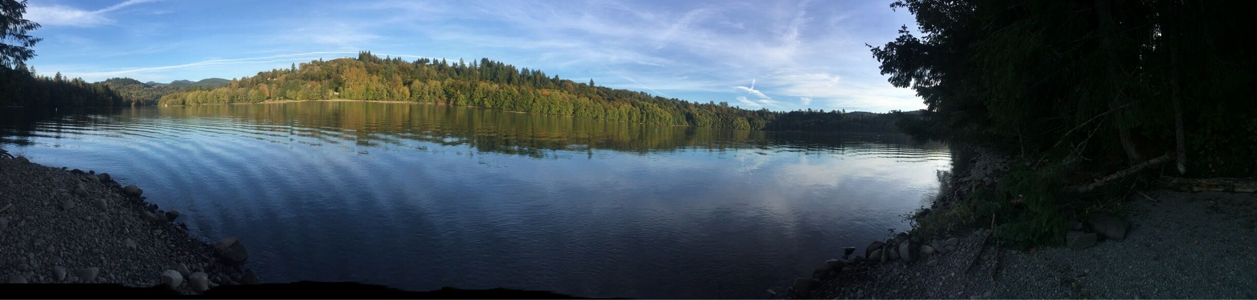 A calm lake with a forested island in the center, surrounded by rocky shores.