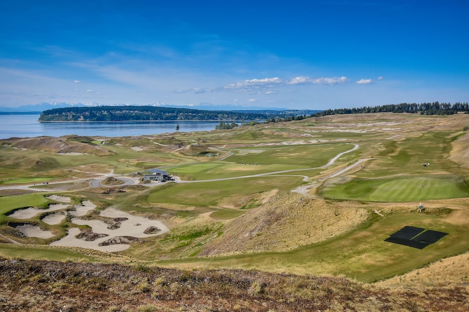 En golfbane med bunkers, vand og fjerne bjerge.
