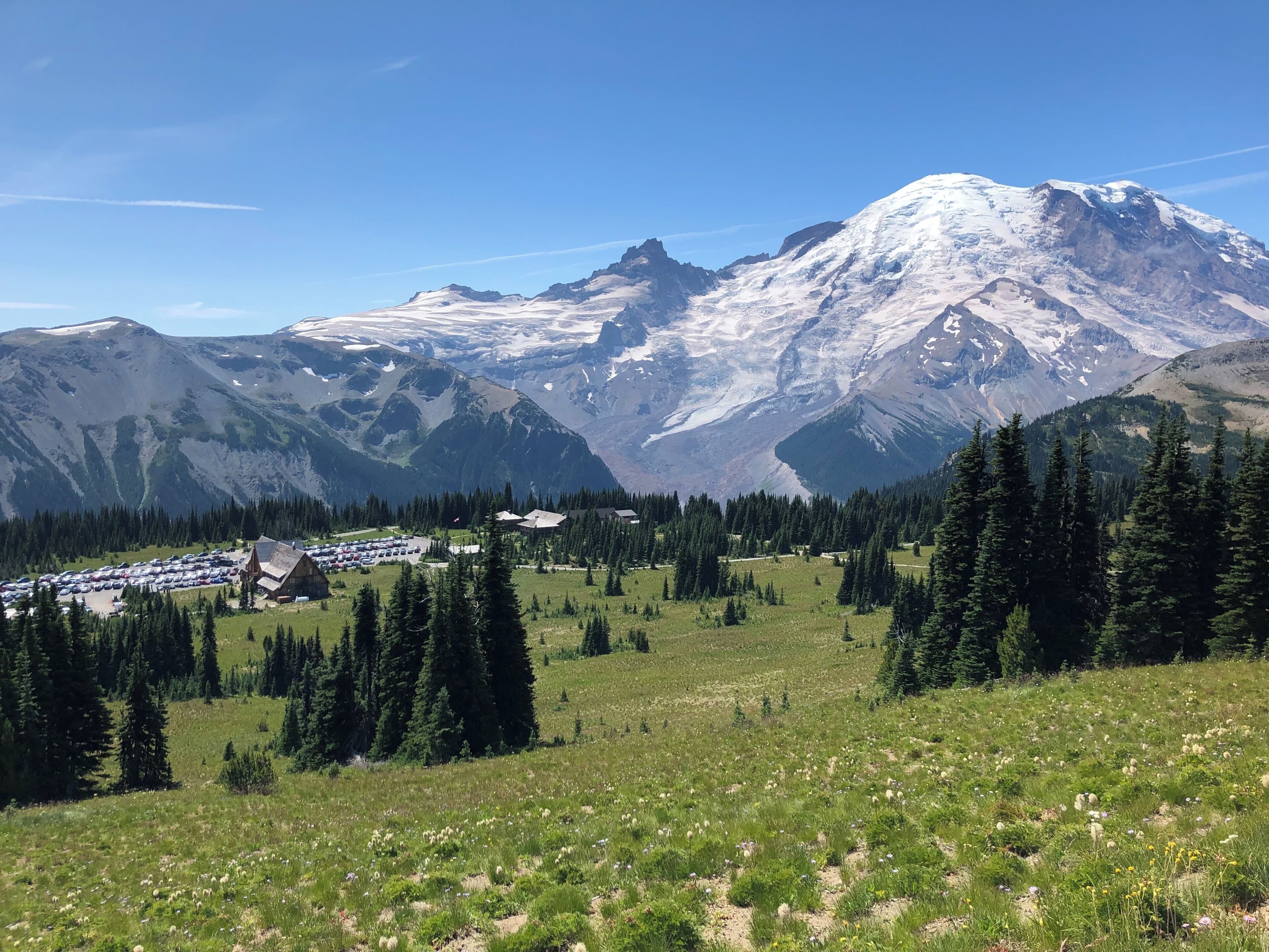 A snow-capped mountain range, a parking lot, and a forested area.