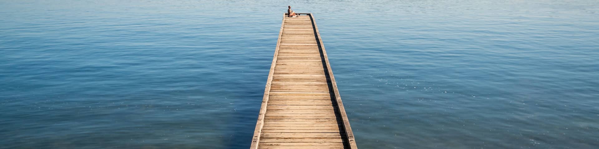 A wooden pier extending into calm waters with a city skyline in the background.