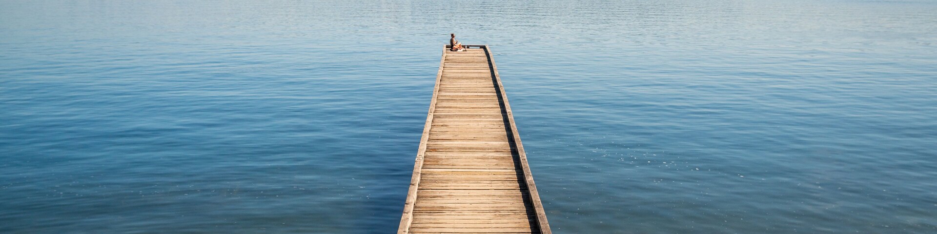 Un muelle de madera que se adentra en aguas tranquilas, con el perfil urbano de una ciudad al fondo.