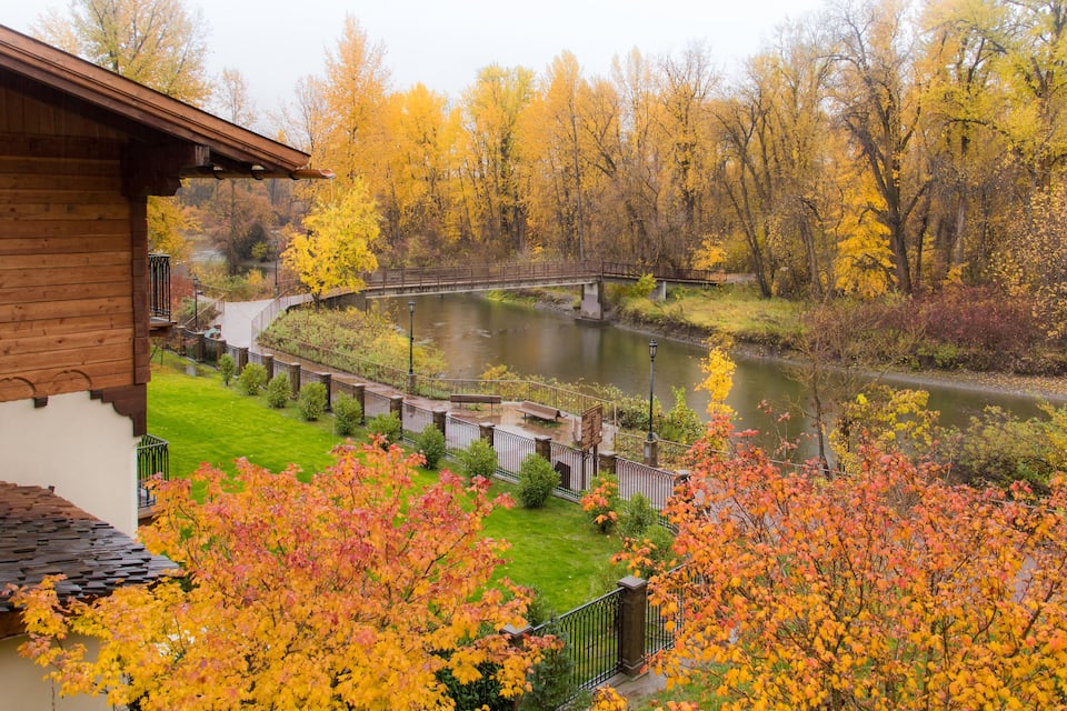 A riverside view with autumn foliage, a wooden building, and a bridge.