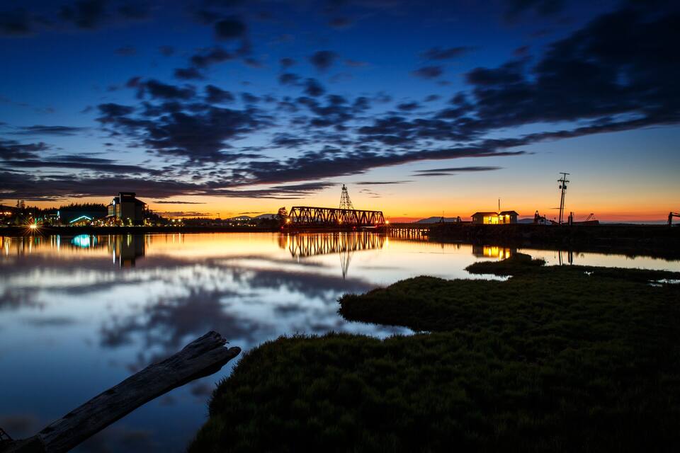 A sunset over a calm lake with a bridge and buildings reflecting on the water.