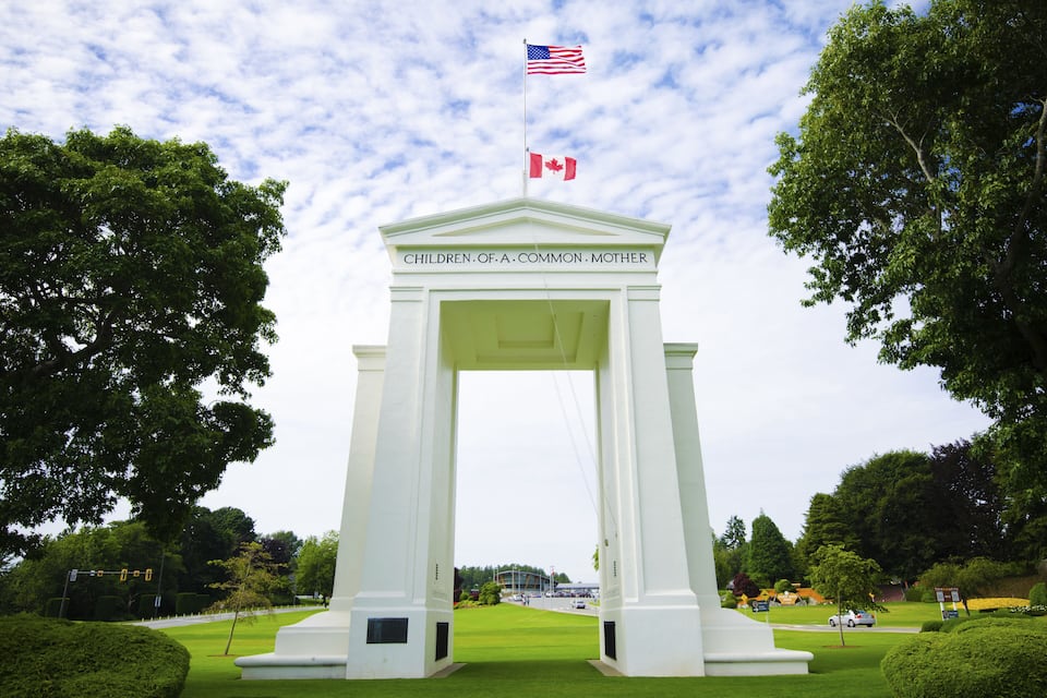 A white monument with the inscription "Children of a Common Mother" and flags of the USA and Canada.