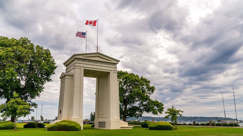 A monument with inscriptions, surrounded by well-maintained grass and trees, under a cloudy sky.