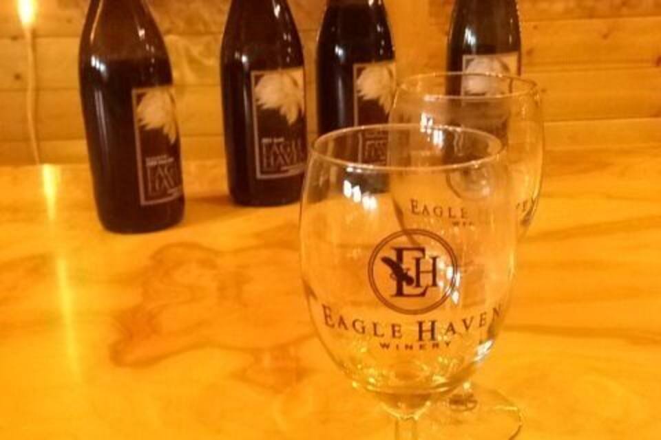 Un got amb la inscripció "Eagle Haven Winery", envoltat de botelles de vi.