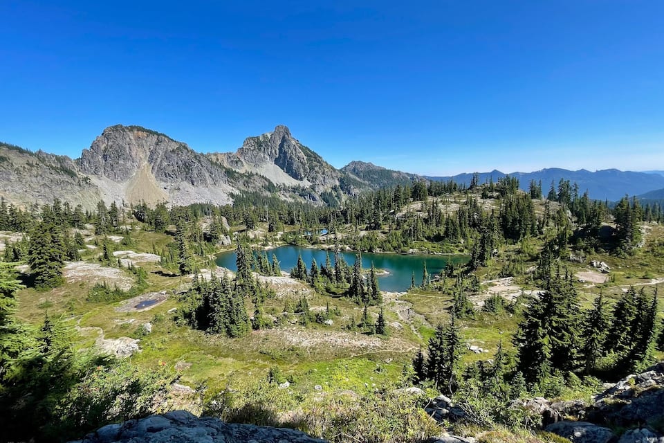 A mountainous landscape with a lake surrounded by dense forests and rocky terrain.