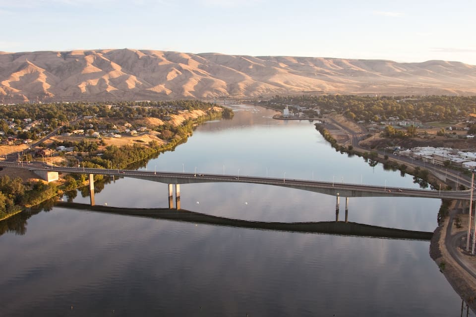 A river with a bridge, surrounded by hills and a clear sky.
