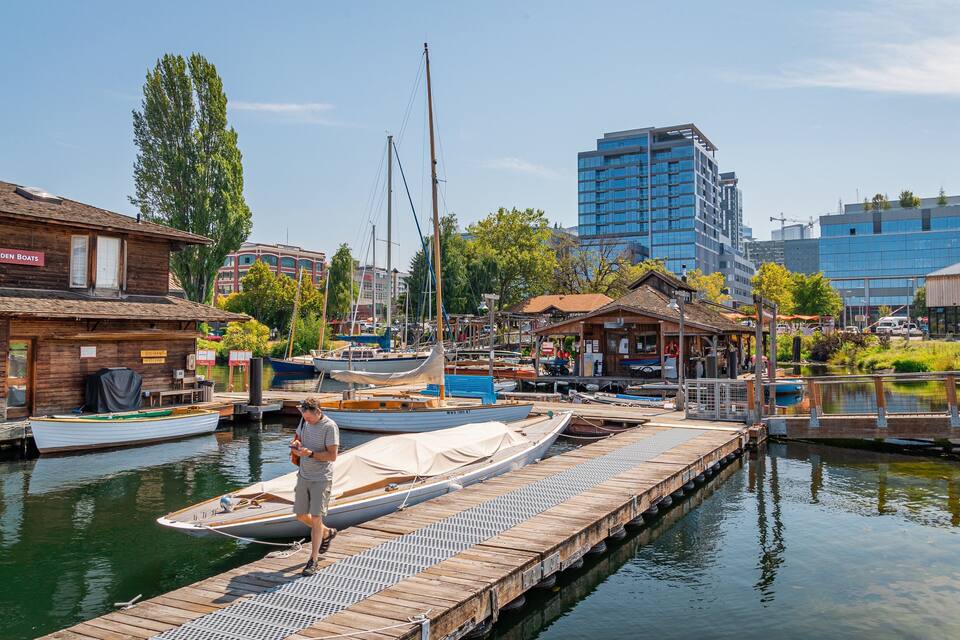 Une jetée en bois avec des bateaux, un bâtiment en bois portant l’inscription « Le Centre des bateaux en bois », et des bâtiments modernes en arrière-plan.