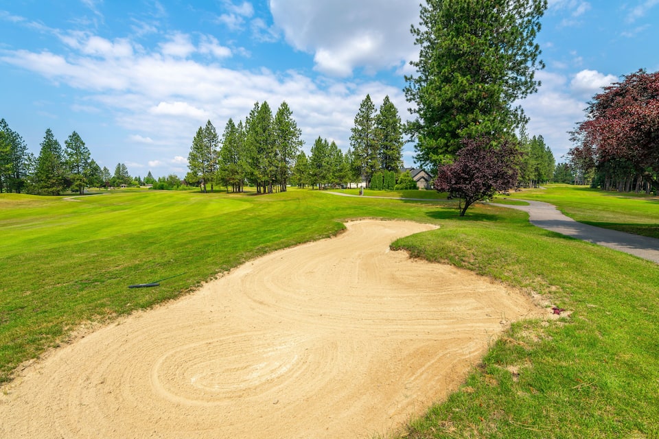 A golf course with a sand bunker, green grass, trees, and a clear sky.