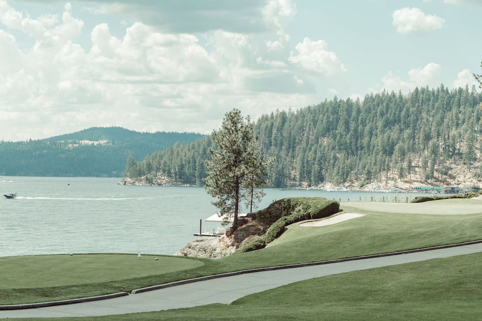 A golf course with a lake, trees, and a distant mountain range.