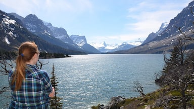 A woman overlooking a calm lake surrounded by snow-capped mountains.