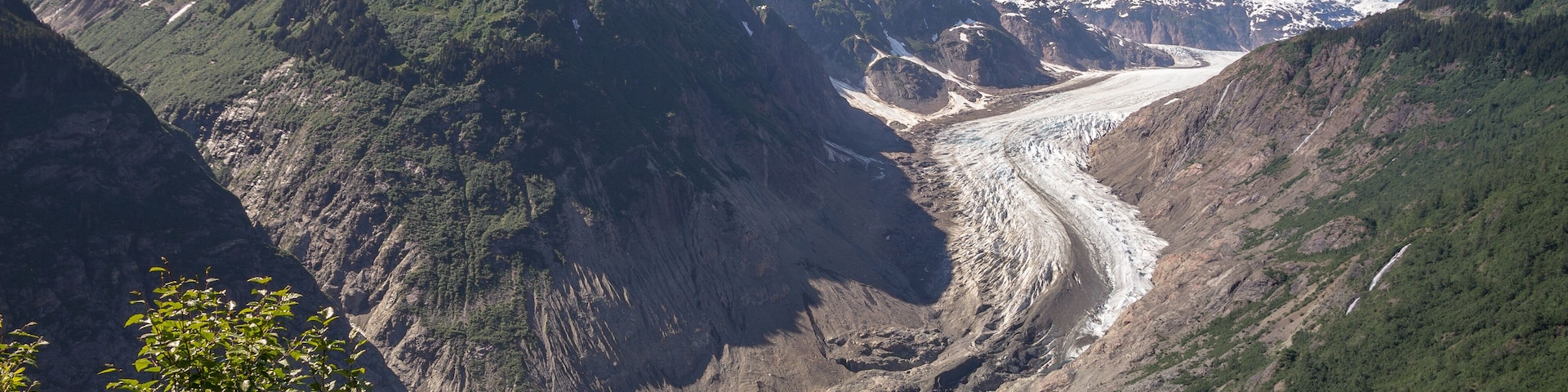 Une vallée glaciaire, avec des montagnes aux sommets enneigés et une riviÚre qui la traverse.