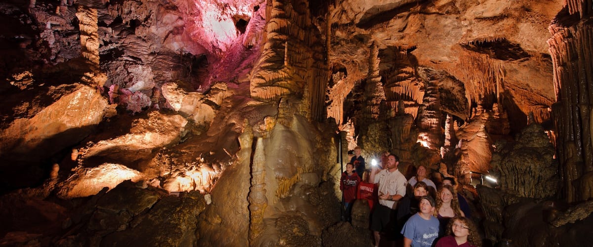 Eine Gruppe von Menschen in einer Höhle mit Stalaktiten und einem rötlichen Schein.