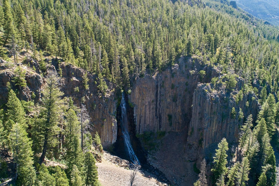Un cañón con una cascada rodeada de bosque denso.