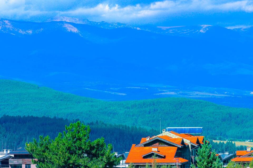A mountainous landscape with a clear sky, green fields, and buildings with orange roofs.