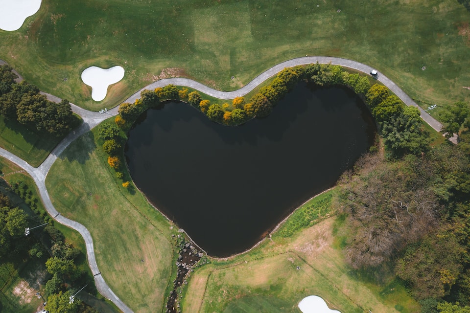 An aerial view of a heart-shaped lake surrounded by a winding road and greenery.