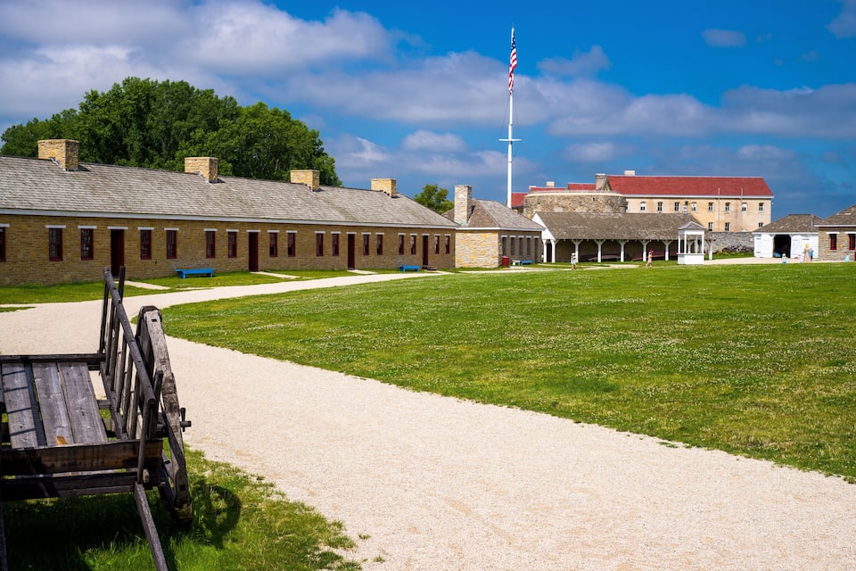 A historic building with a red roof, a flagpole with an American flag, and a wooden cart in the foreground.