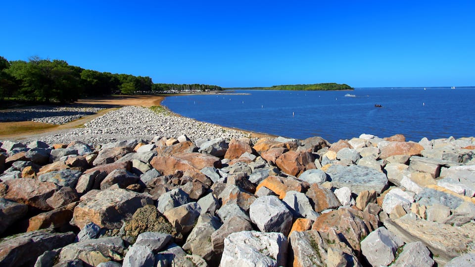 A rocky shoreline with a clear blue sky and calm water.