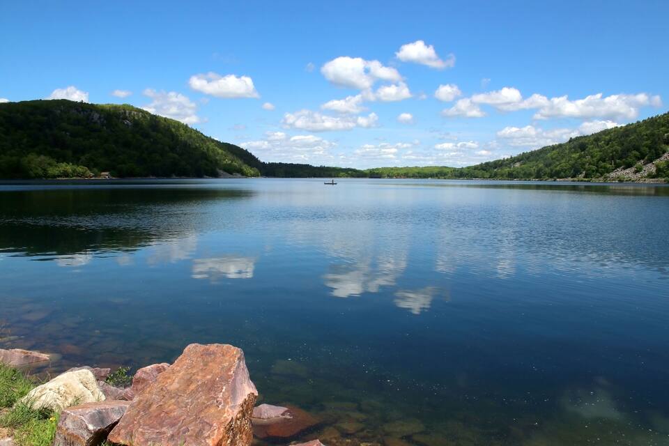 A calm lake with clear water, surrounded by green hills and a small boat in the distance.