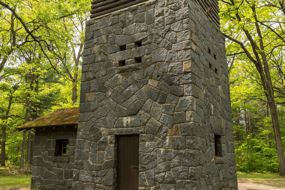 Edificio de piedra con sección superior de madera, rodeado de frondosos árboles verdes.